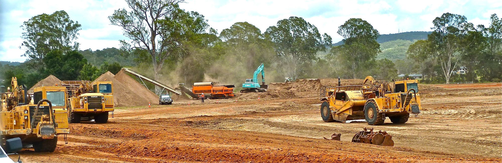 Illustrative earthmoving scrapers and an excavator working a wide open construction site, not an actual project
